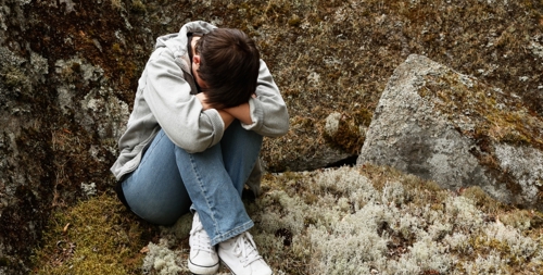 Ett ledset barn som sitter på en mossbeklädd sten