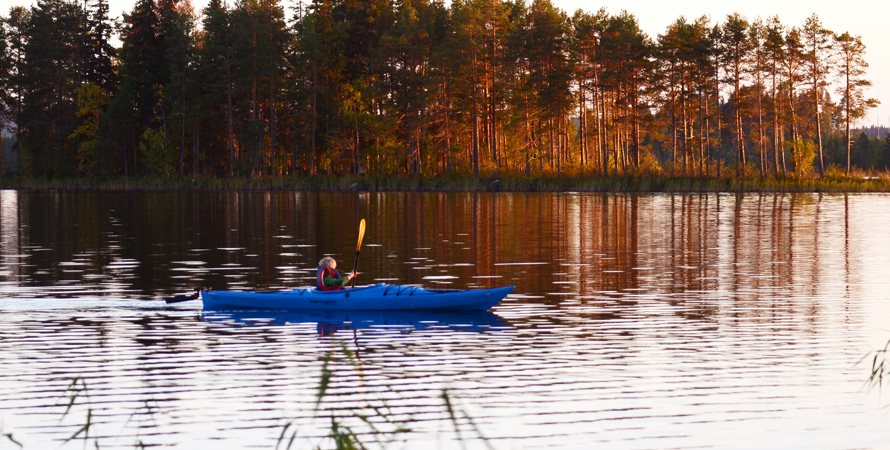 En person sittandes i en blå kanot på en sjö. I bakgrunden ser man en ö med träd på