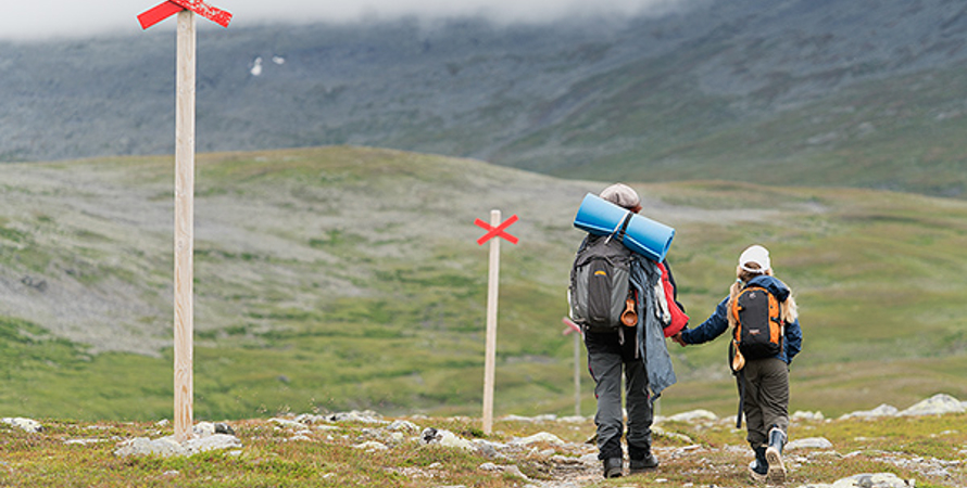 Två personer med ryggsäck på sig som går efter en vandringsled på fjället. 