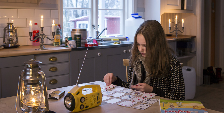Ett barn spelar kort i ett kök utan ström med levande ljus som belysning